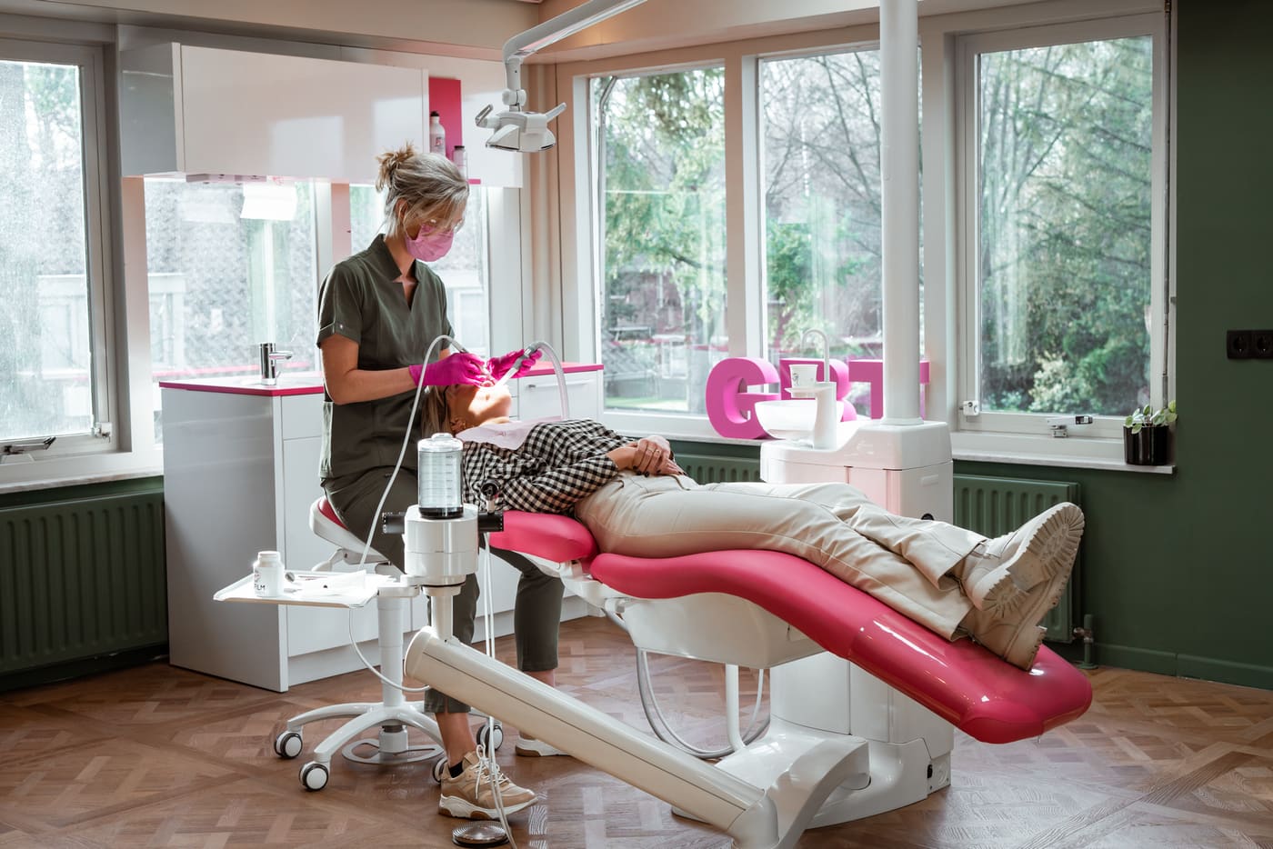 Mondhygiënist behandelt een patiënt in de roze behandelstoel